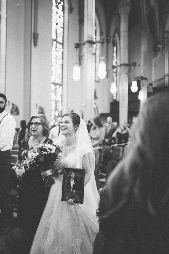 bride walking down the aisle with her mom and a photo of her dad