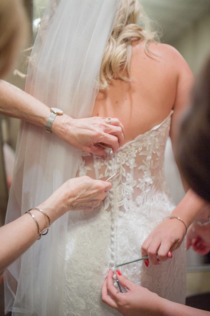 bride getting her dress on, close up of the hands on the back of her dress