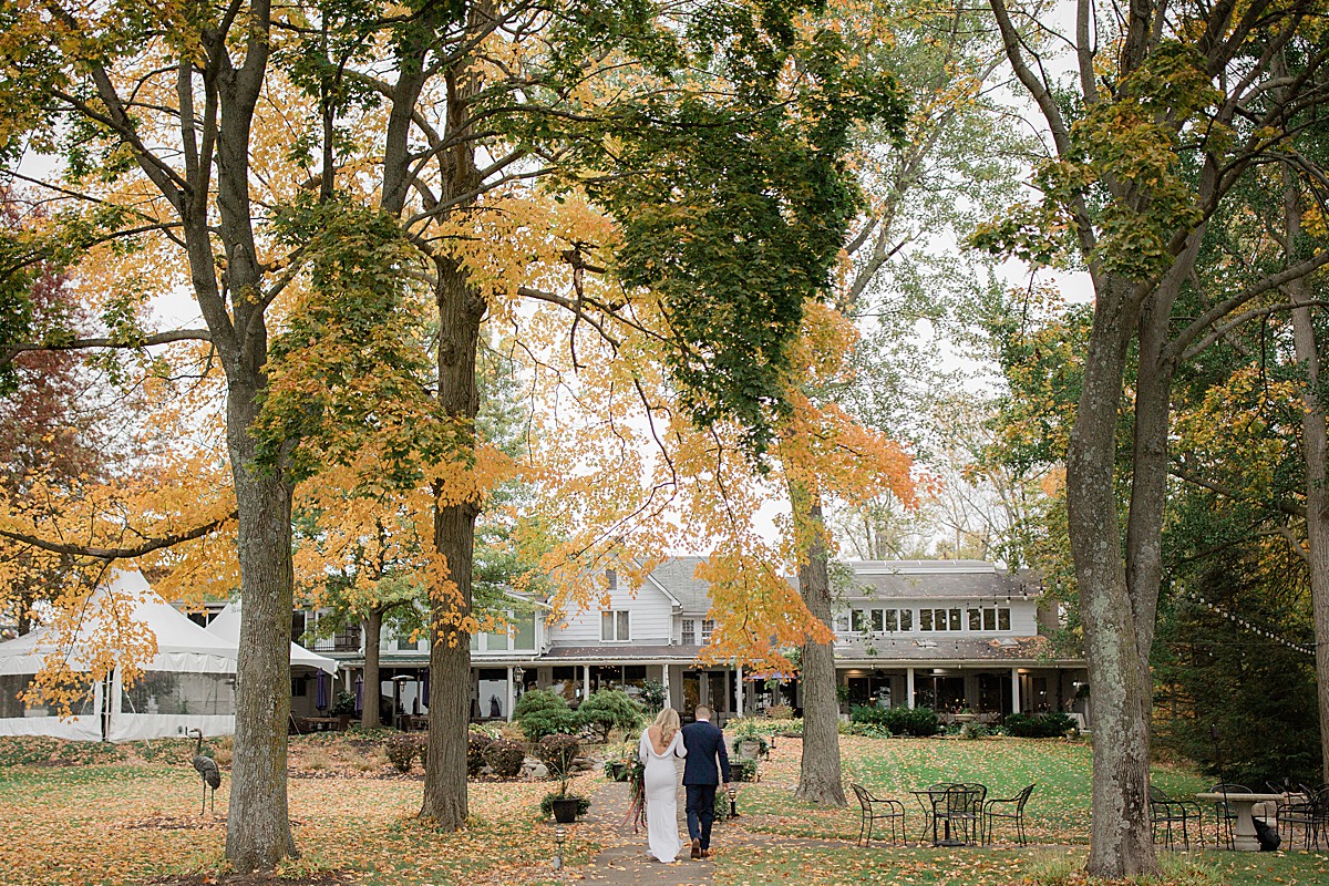 bride and groom walking back toward the restaurant with fall leaves everywhere